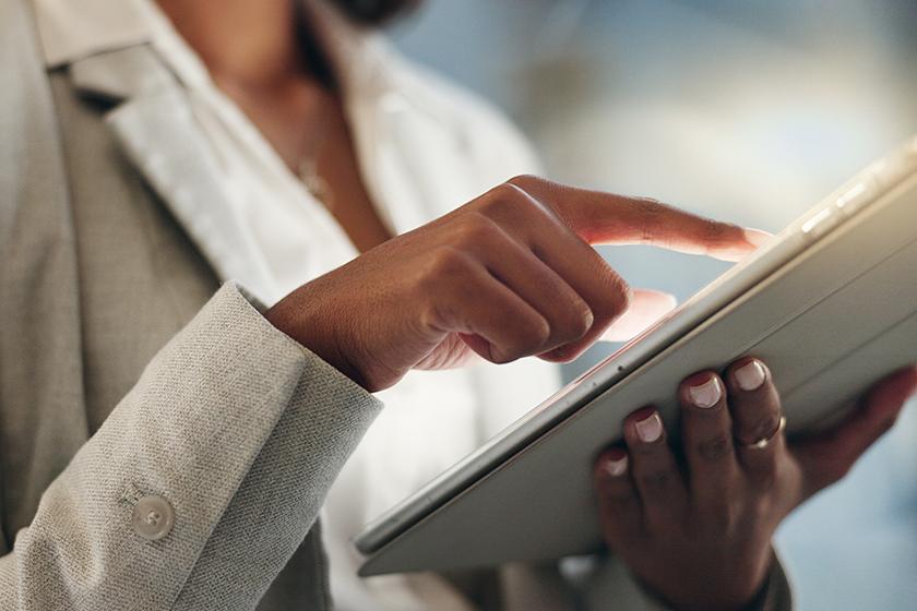 Business woman wearing a beige jacket holding a tablet in her hands.