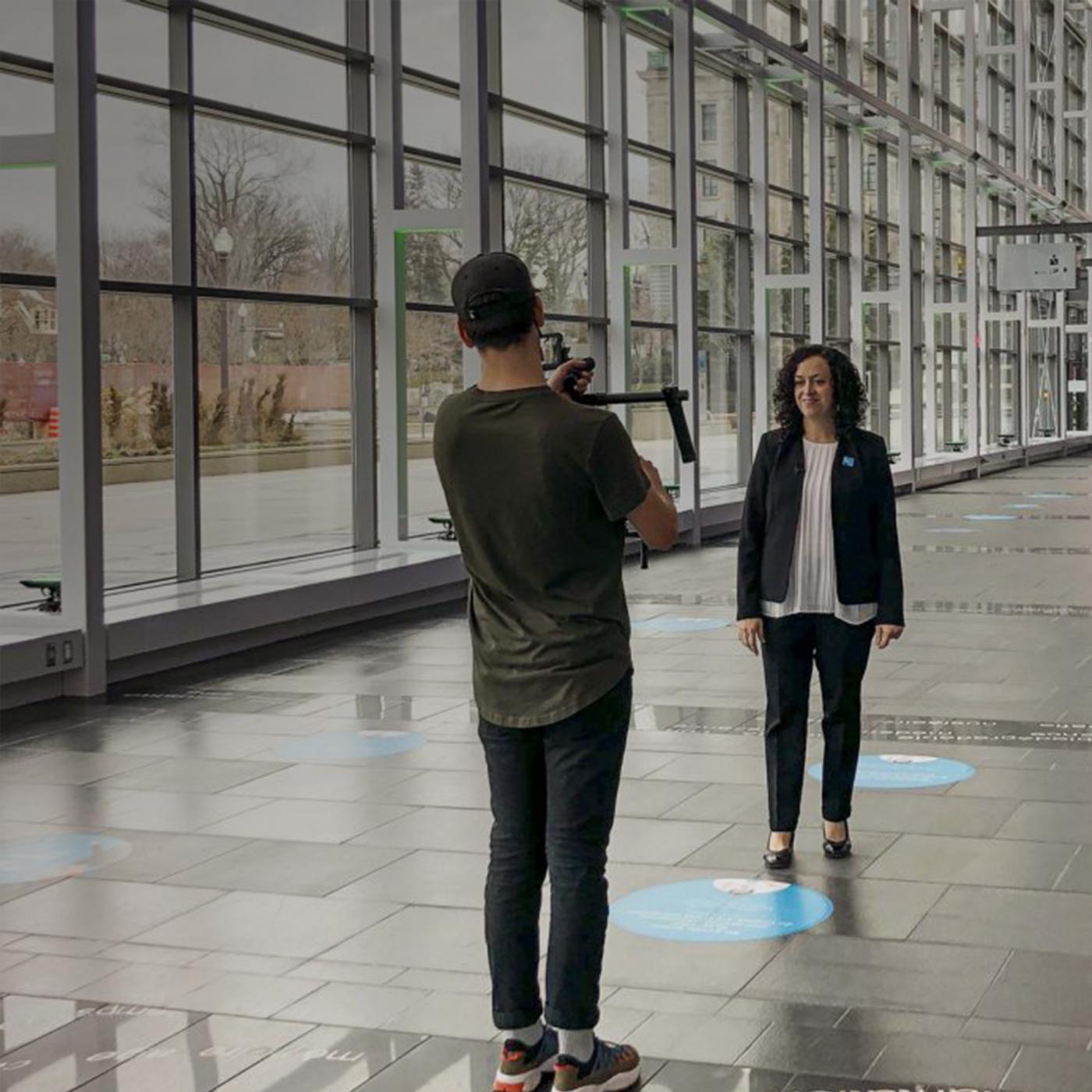 Picture of one woman preseneting for a vitual visiting broadcast and a man filming and holding a camera.