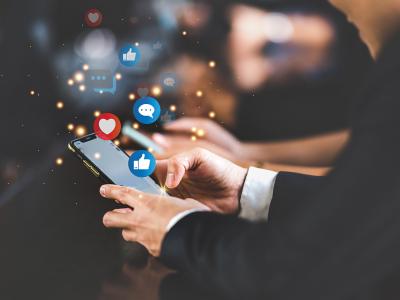 Business man holding a phone in his hands, with likes and thumbs-up social media icons flying around